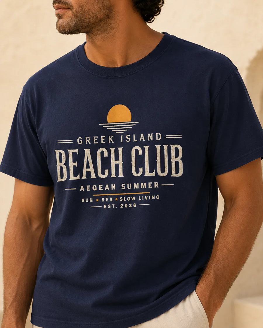 Man wearing a navy “Greek Island Beach Club” T-shirt with a vintage Mediterranean resortwear graphic.