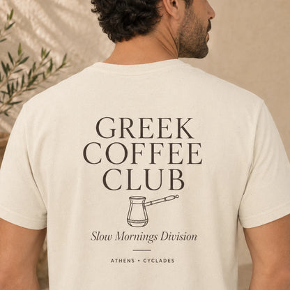 TP HERO: A man shown from the back wearing a cream-colored t-shirt with a black graphic print that reads 'GREEK COFFEE CLUB' and 'Slow Mornings Division'.