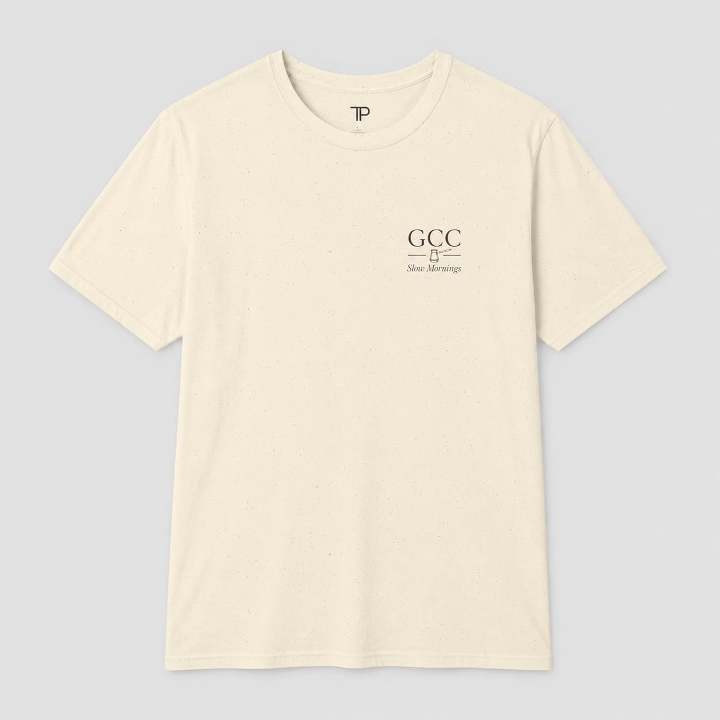 An off-white crewneck t-shirt with a small black graphic on the left chest reading 'GCC New Meersburg' and a small 'TP' logo inside the collar, displayed on a neutral gray background.