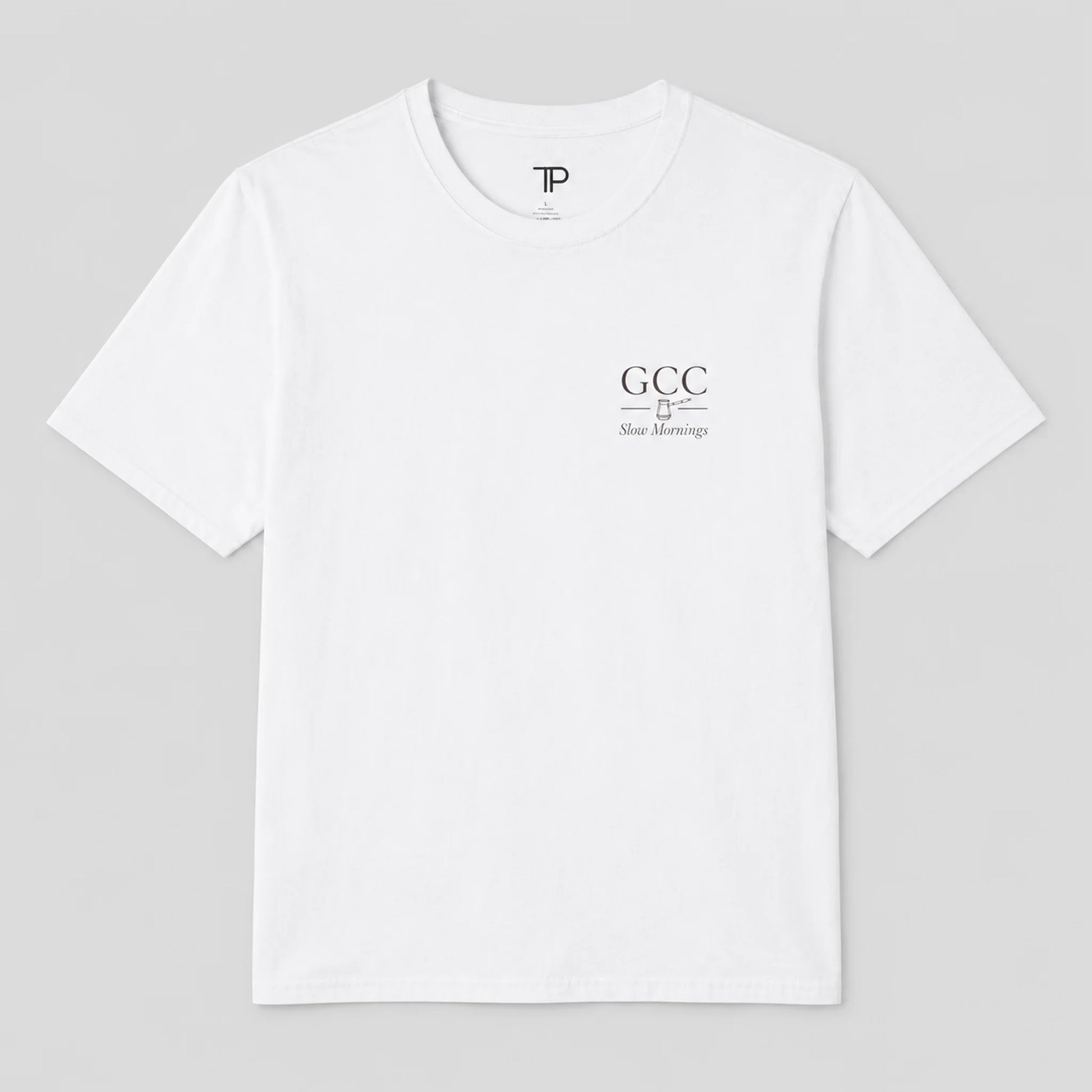 A white crewneck t-shirt with a small black graphic on the left chest reading 'GCC New Meersburg' and a small 'TP' logo inside the collar, displayed on a neutral gray 
