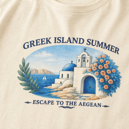 Close-up of an off-white speckled T-shirt with a colorful graphic print depicting a Greek island scene with a white building, blue dome, ocean, flowers, and the text 'GREEK ISLAND SUMMER' and 'ESCAPE TO THE AEGEAN'.