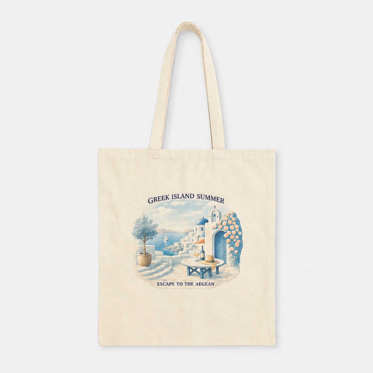 A cream-colored canvas tote bag with a vintage-style illustration of a Greek island summer scene, featuring the text 'GREEK ISLAND SUMMER' and 'ESCAPE TO THE AEGAN'.