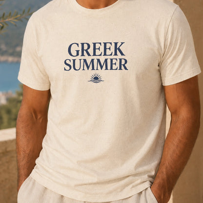 A man wearing a cream-colored t-shirt with 'GREEK SUMMER' printed in navy blue text and a small sun-and-wave graphic below it, set against a blurred outdoor background.