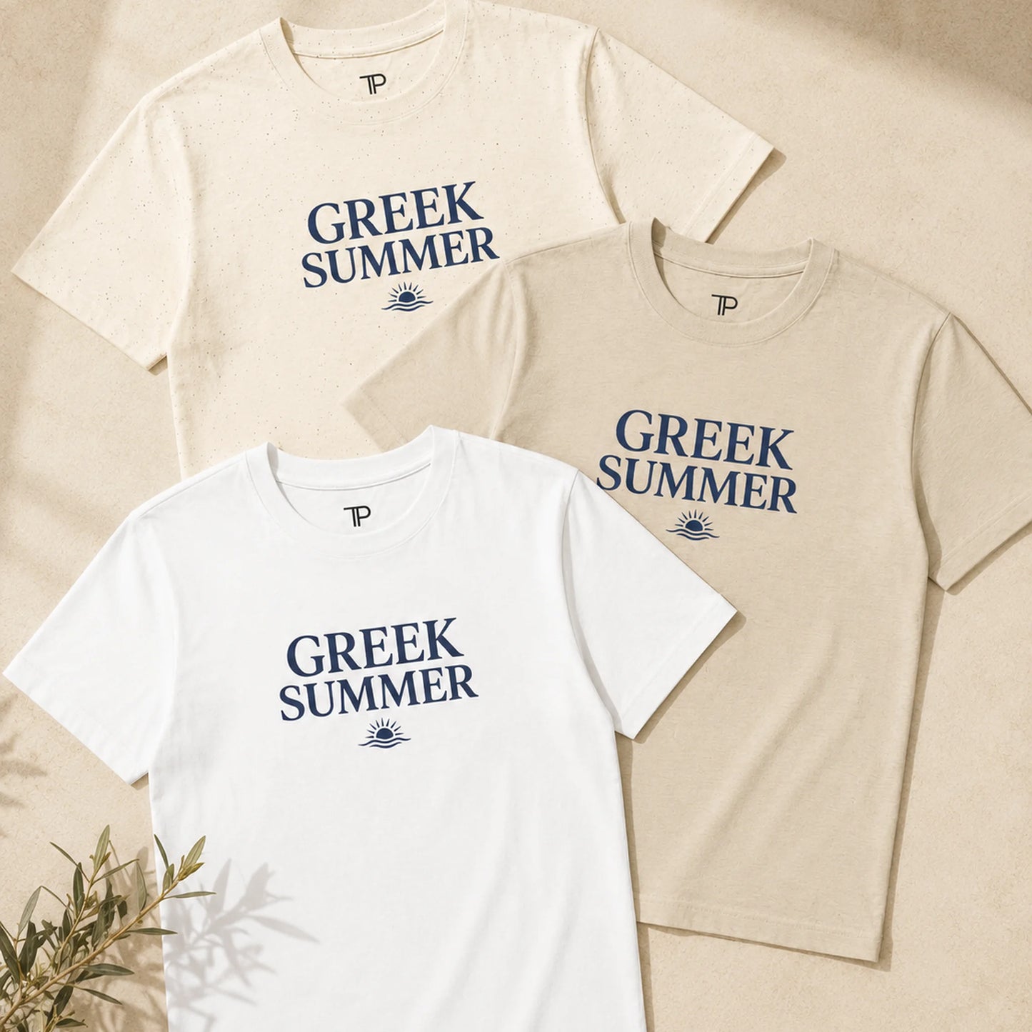 Three short-sleeve crew-neck T-shirts in white, beige, and cream, each printed with the words 'GREEK SUMMER' in navy blue and a small sun-and-eyes graphic below. The shirts are arranged on a warm beige textured background with a small plant sprig in the lower left corner.