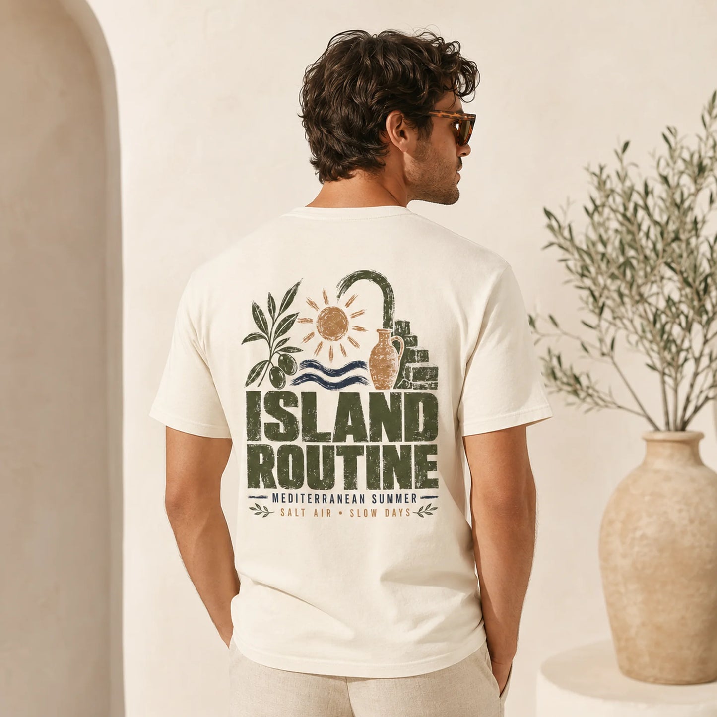 Man wearing a white t-shirt with 'Island Routine' design, standing in a minimalistic indoor setting.