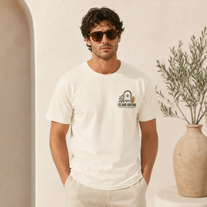 Man wearing a white t-shirt with a logo, standing in a neutral setting with a vase and plant.