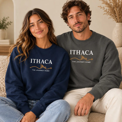 A man and a woman sitting together on a couch wearing matching crewneck sweatshirts. The woman wears a navy blue sweatshirt with white and gold text reading 'ITHACA THE JOURNEY HOME', and the man wears a dark gray sweatshirt with the same design.