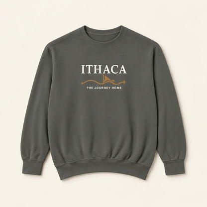 A dark gray crewneck sweatshirt with 'ITHACA' and 'THE JOURNEY HOME' embroidered in white on the chest, accented by a small orange graphic, shown against a light beige background.