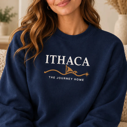 TP HERO: A woman wearing a navy blue crewneck sweatshirt with a white and gold graphic that reads 'ITHACA THE JOURNEY HOME' on the chest, shown in a cozy indoor setting.