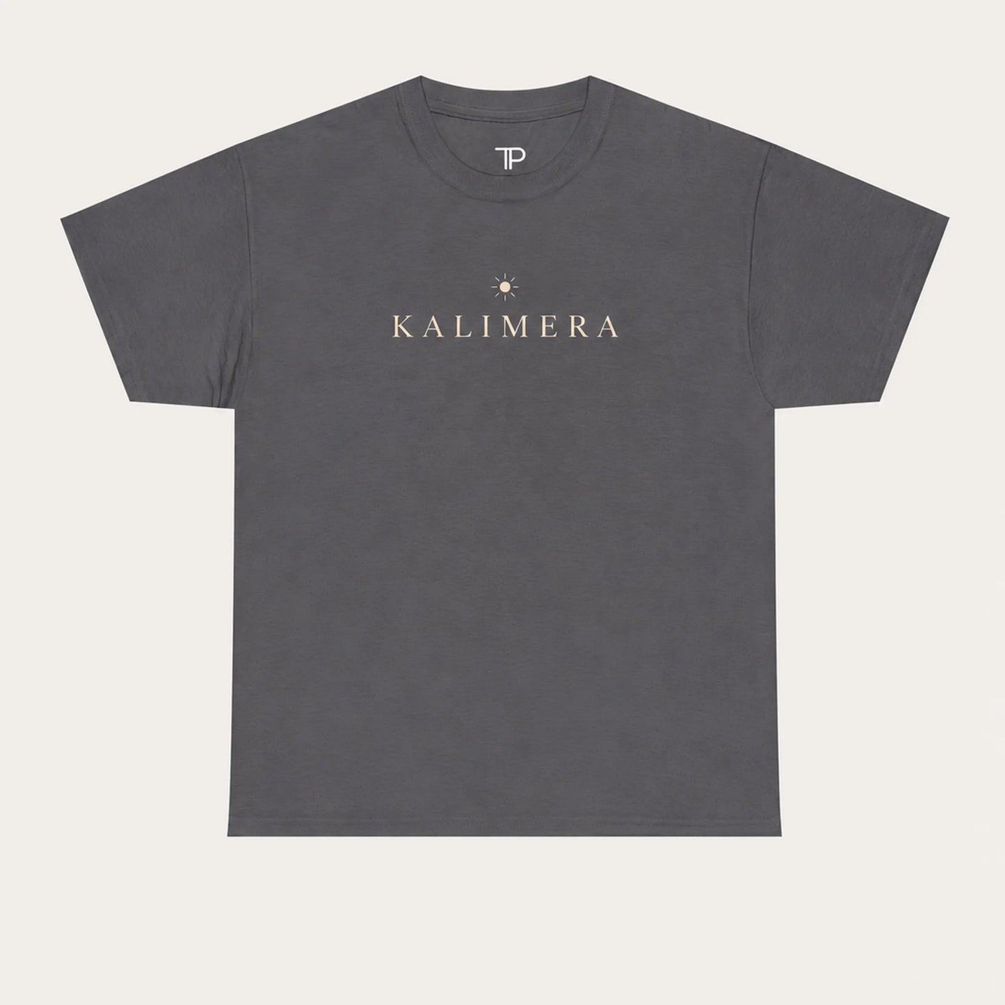 A charcoal crewneck t-shirt with 'KALIMERA' printed in beige across the chest, accompanied by a small star graphic, shown on a light beige background.