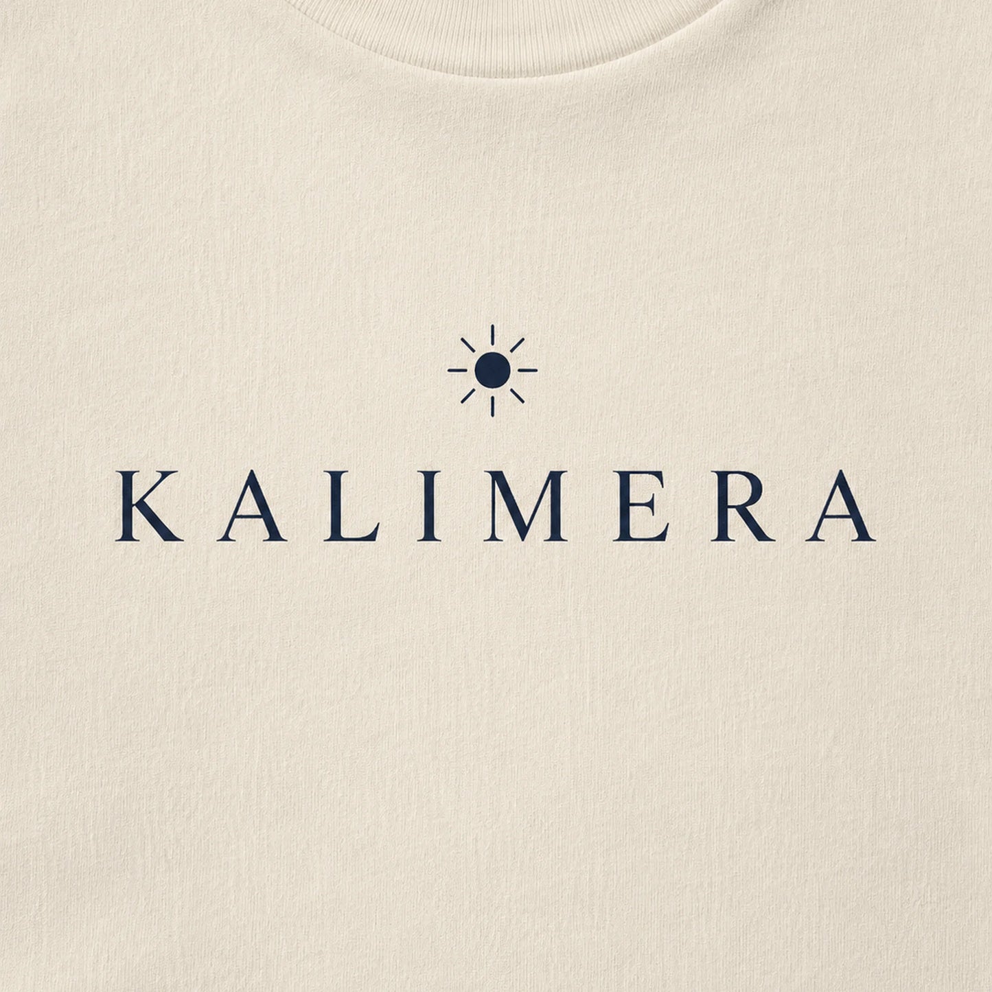 Close-up of a natural-colored crewneck sweatshirt featuring the brand name 'KALIMERA' in navy blue serif lettering with a small sun icon above it.