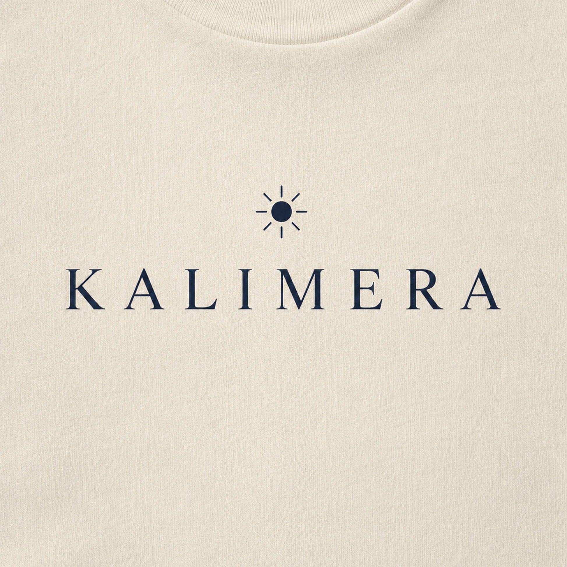 Close-up of a natural-colored crewneck sweatshirt featuring the brand name 'KALIMERA' in navy blue serif lettering with a small sun icon above it.