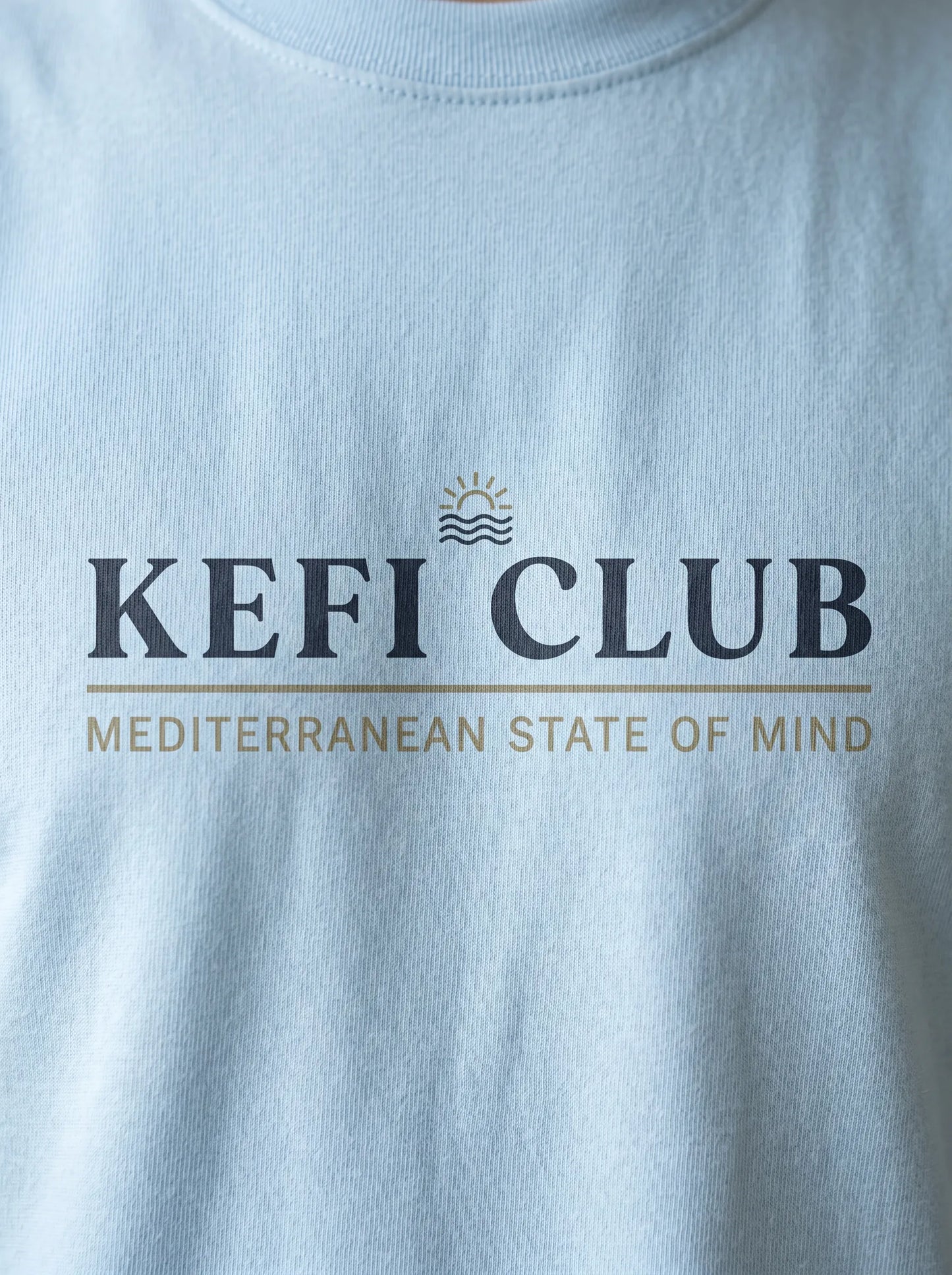 Light blue t-shirt with 'KEFI CLUB' logo and text on a plain background