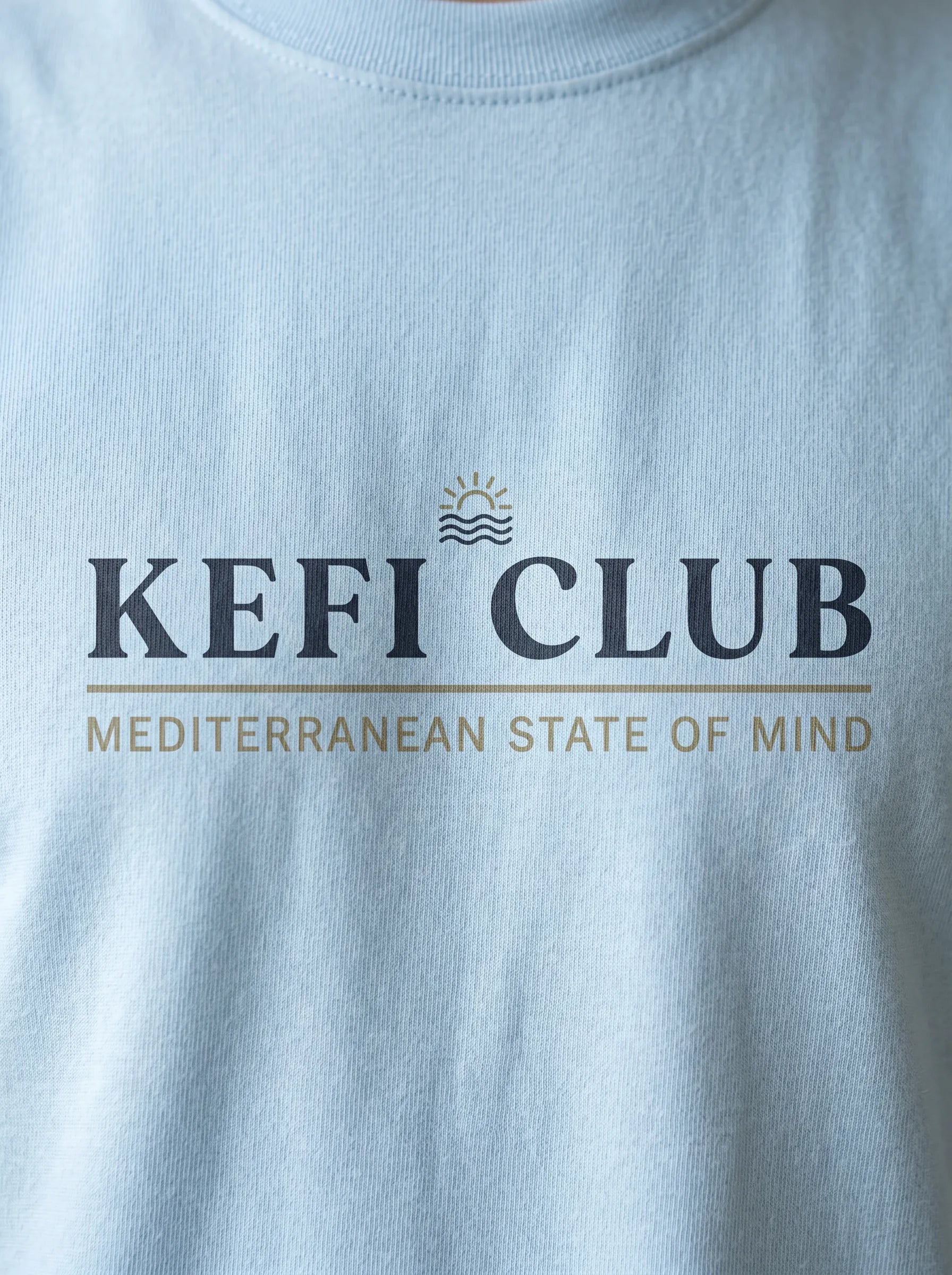 Light blue t-shirt with 'KEFI CLUB' logo and text on a plain background
