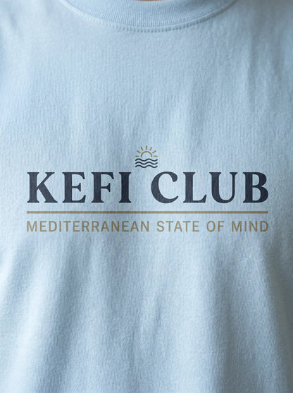 Light blue t-shirt with 'KEFI CLUB' logo and text on a plain background