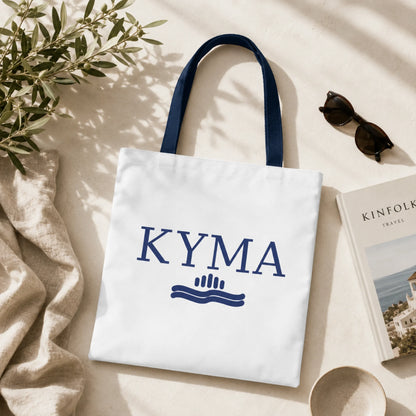 White tote bag with 'KYMA' branding on a light surface with a plant and sunglasses.