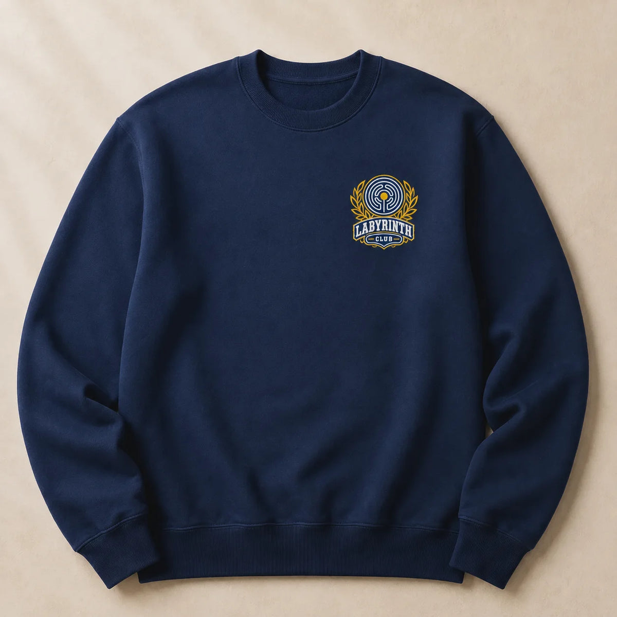 A navy blue crewneck sweatshirt with a small embroidered 'Labyrinth' logo on the left chest, laid flat on a textured beige background.