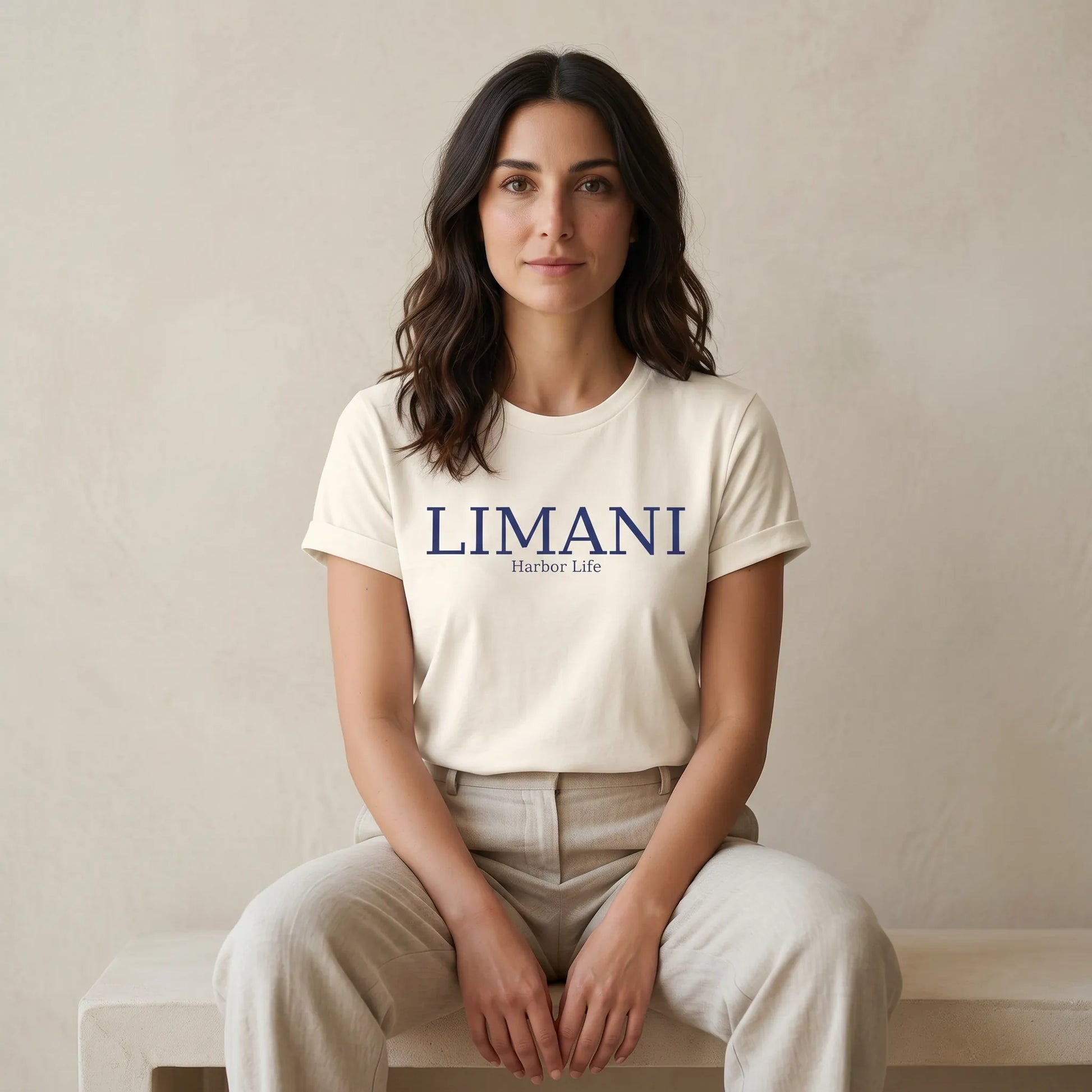 Woman wearing a white t-shirt with 'LIMANI' logo sitting on a bench.
