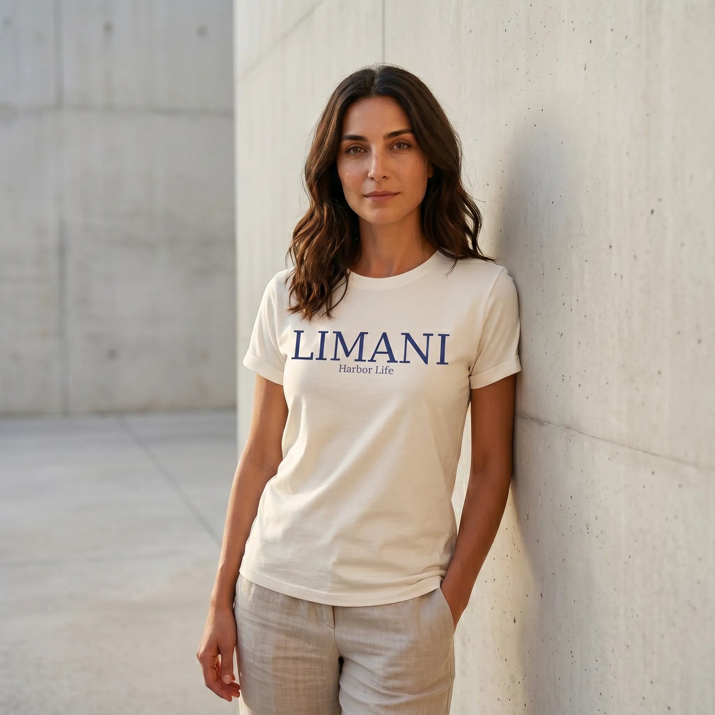 Woman wearing a white t-shirt with 'LIMANI' logo against a concrete wall.
