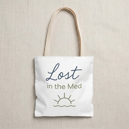 Tote bag with 'Lost in the Med' text and sun icon on a beige background