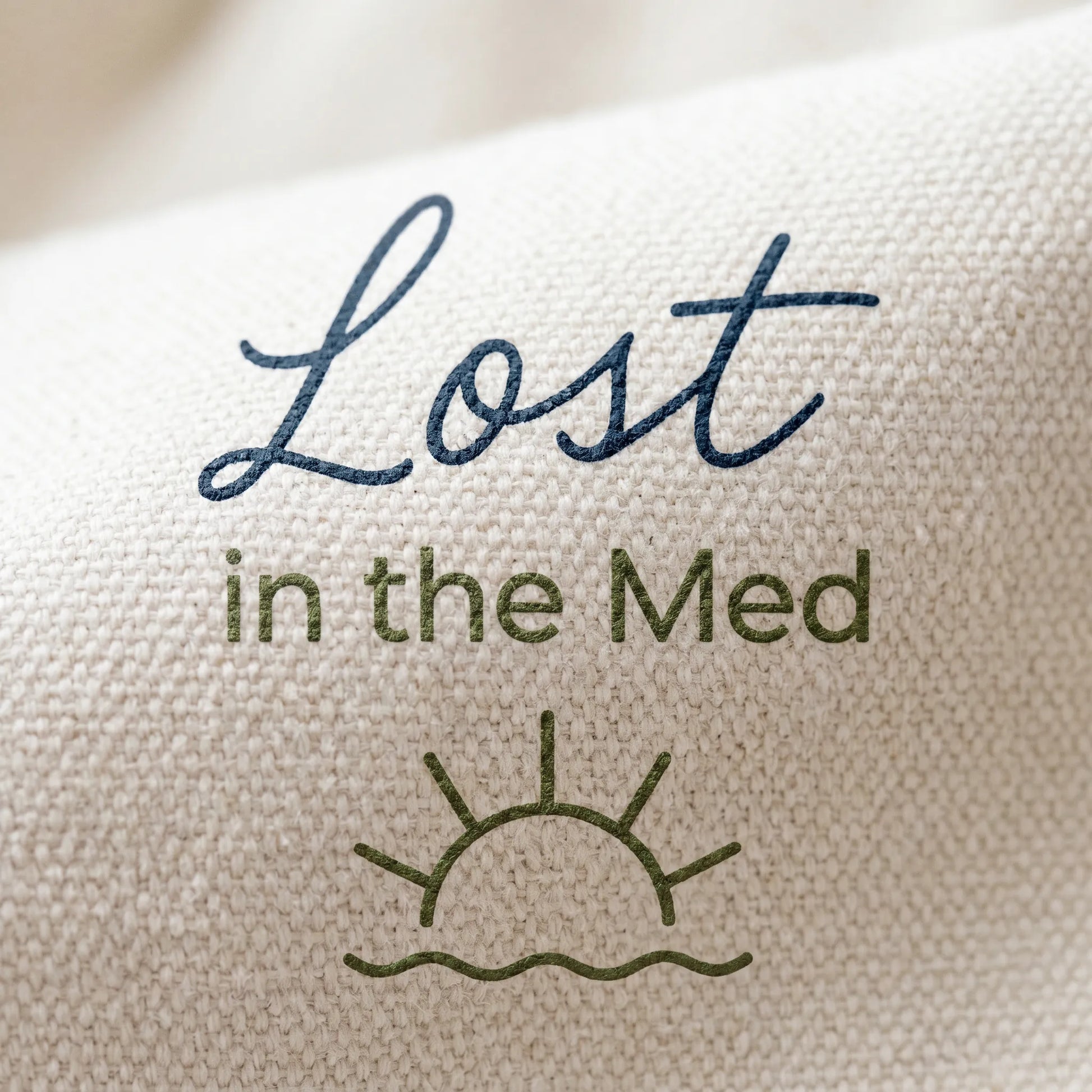 Text 'Lost in the Med' with a sun and wave design on a textured fabric background