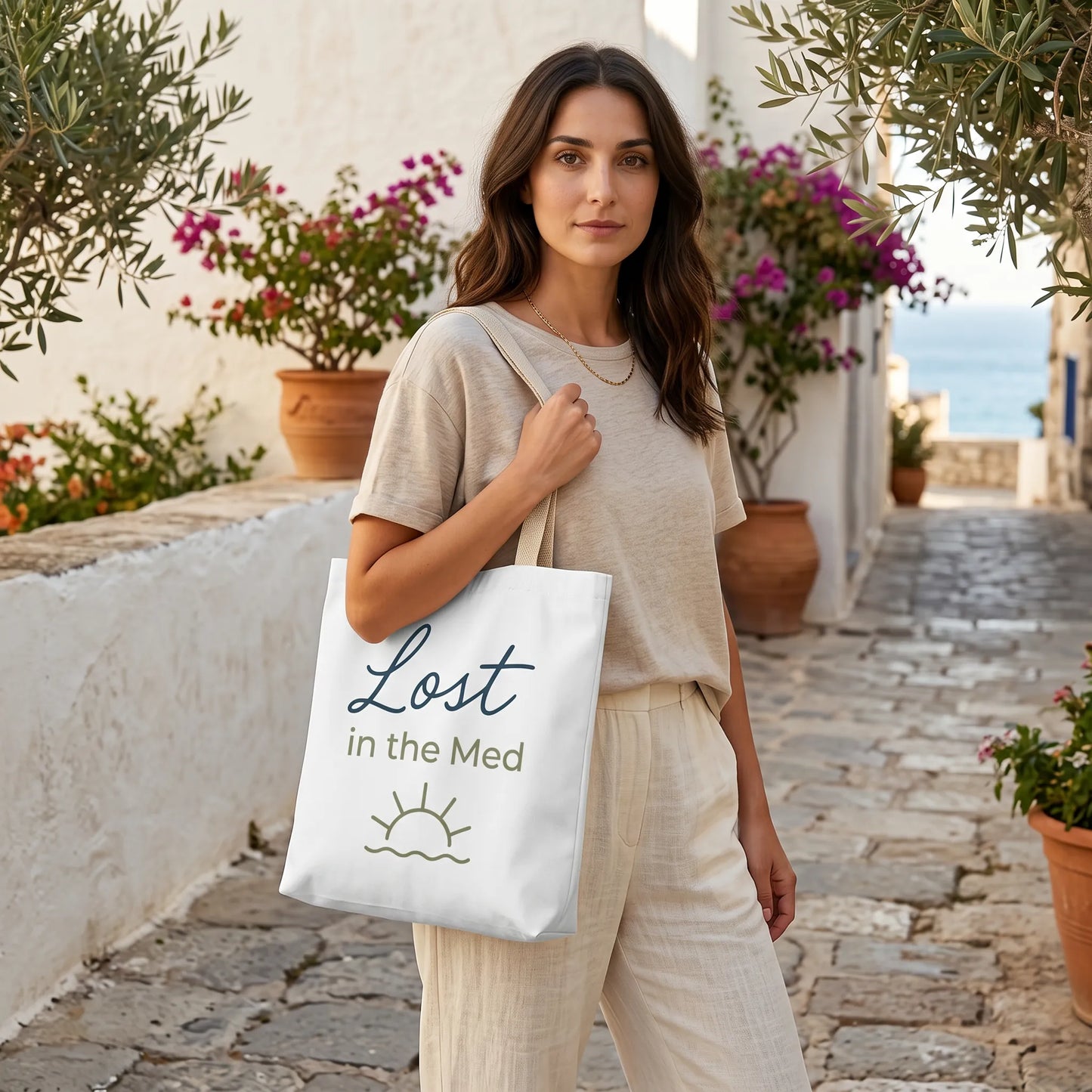 Woman holding a tote bag with 'Lost in the Med' text in a scenic outdoor setting.