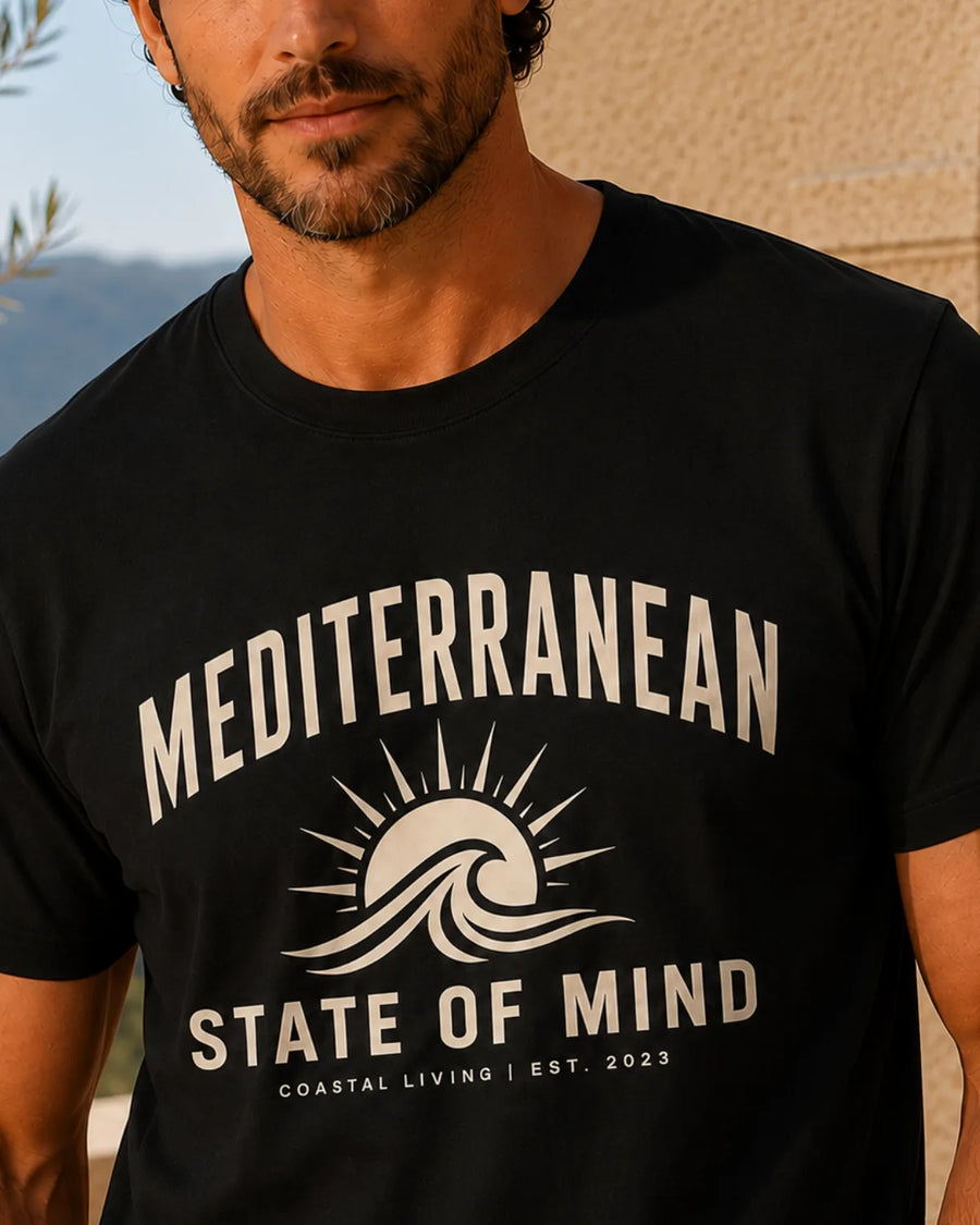 Mediterranean State of Mind black T-shirt with cream sun and wave coastal streetwear graphic on a male model