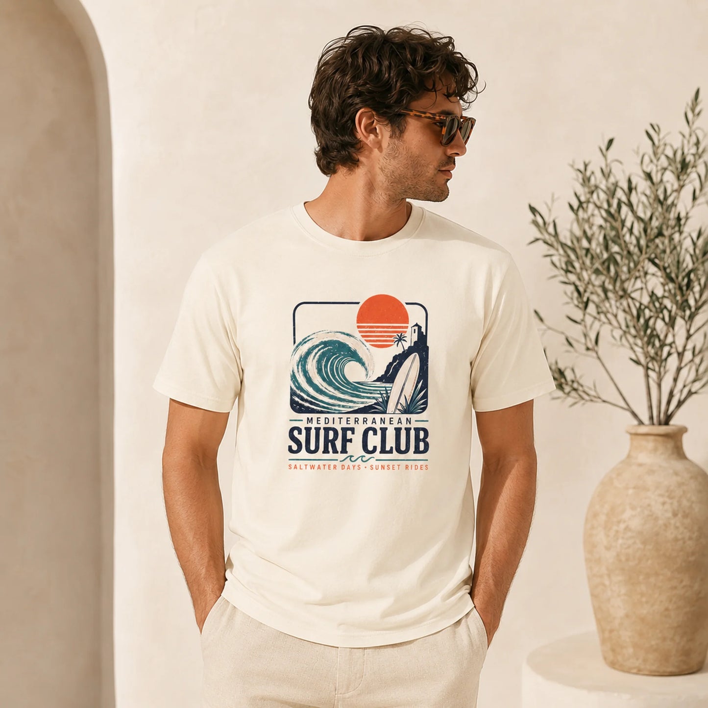 Man wearing a 'Mediterranean Surf Club' t-shirt with a graphic design, standing indoors.