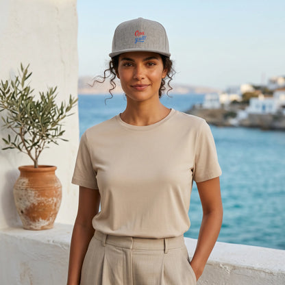 Woman wearing a beige t-shirt and cap by a scenic waterfront.
