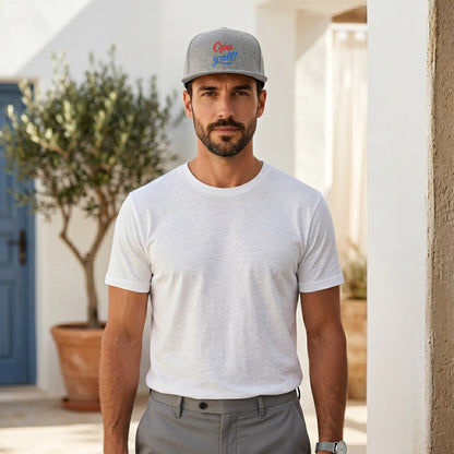 Man wearing a gray cap and white t-shirt standing outdoors.