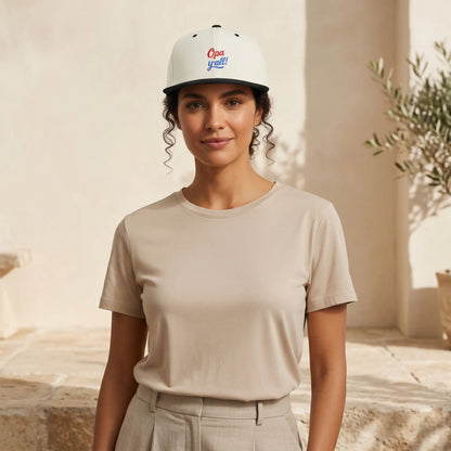 Woman wearing a beige t-shirt and white cap with text, standing in a sunlit outdoor setting.