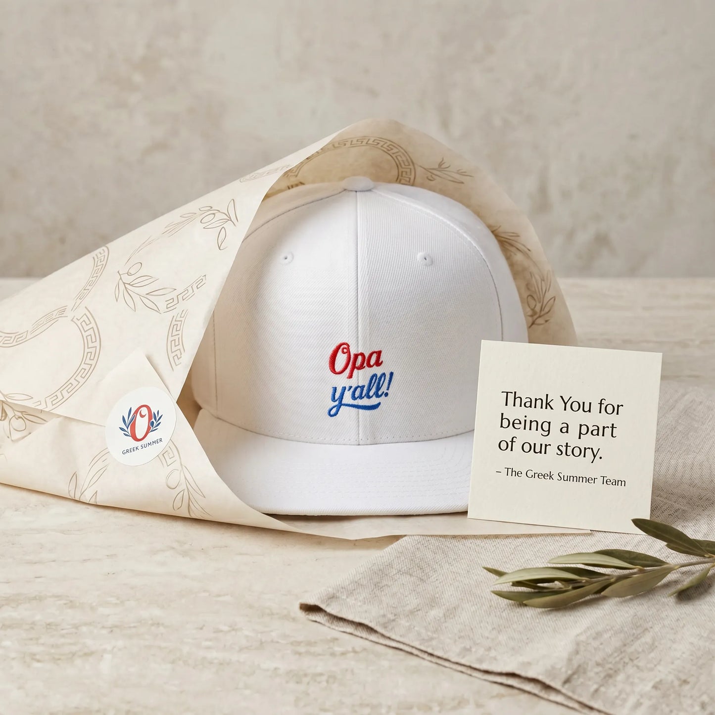 White cap with 'Opa y'all!' text, accompanied by a card and decorative elements on a neutral background
