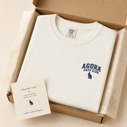 White sweatshirt with 'Agora Cats Club' logo and a card in a cardboard box.