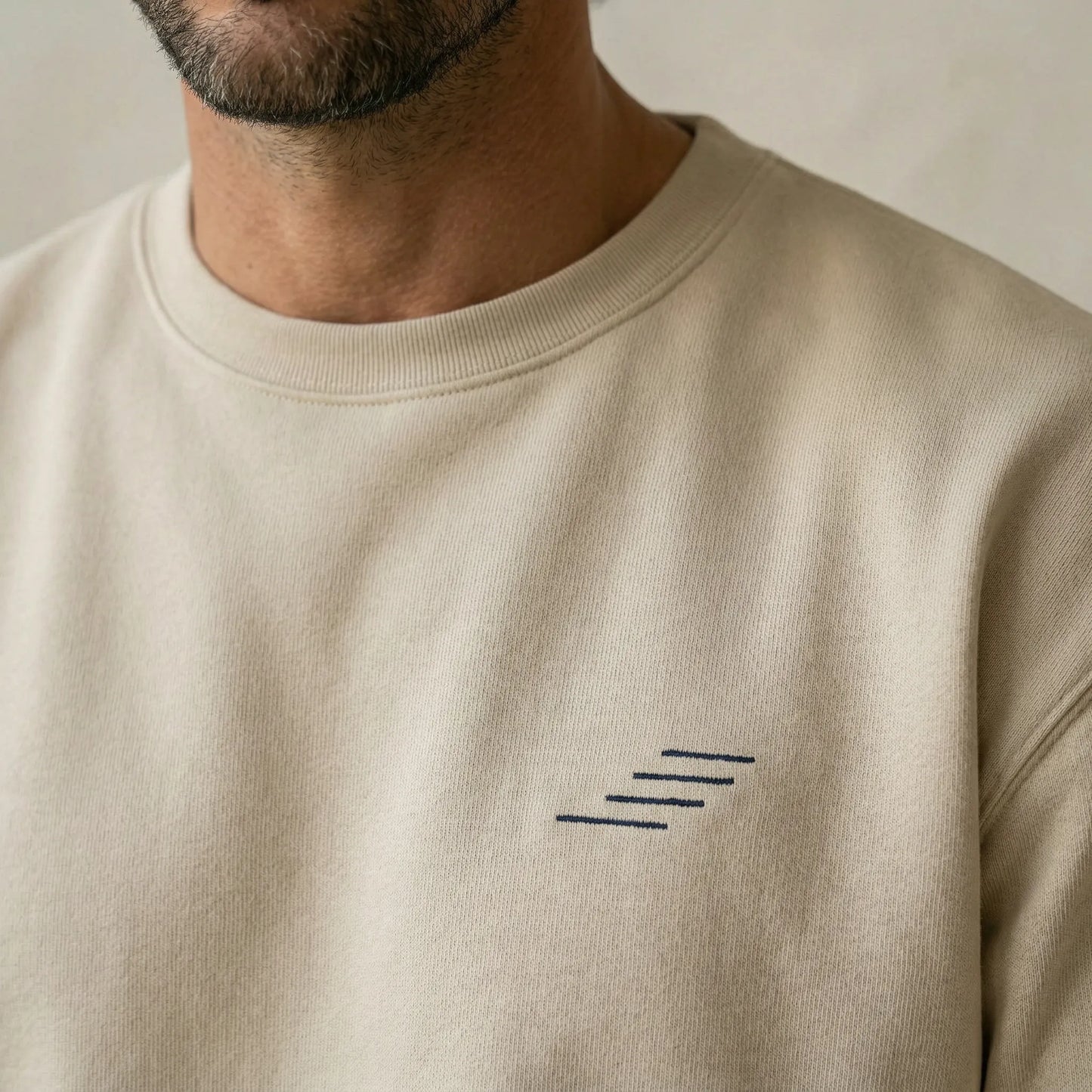 Beige sweatshirt with a small logo on the chest against a neutral background