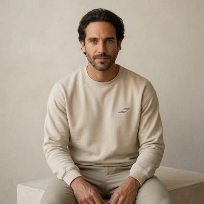 TP HERO: Man wearing a beige sweatshirt with a small logo, sitting on a light-colored surface against a neutral background.
