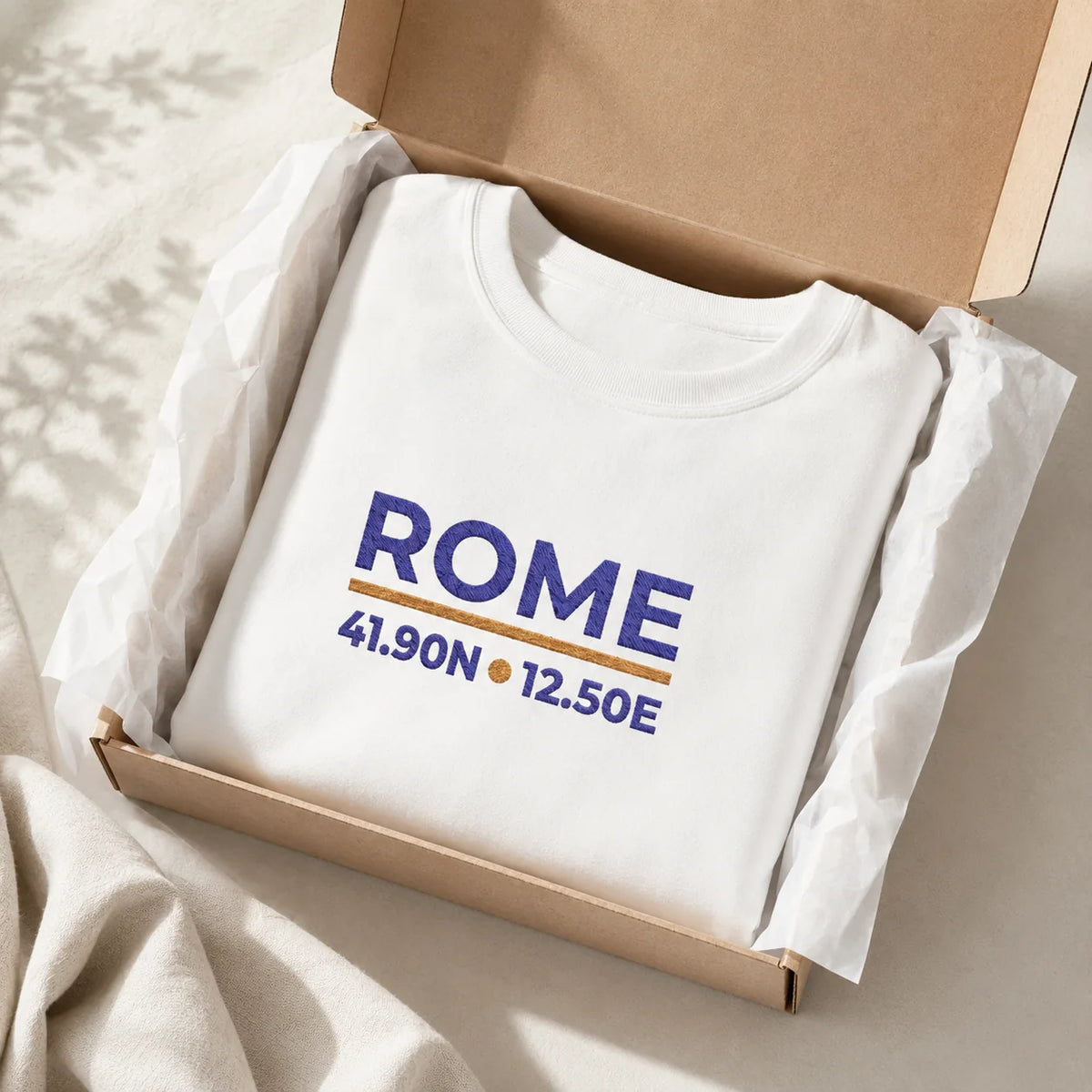 Folded White Rome Coordinates embroidered crewneck sweatshirt with navy and gold city-coordinate design, prepared in gift-style packaging.