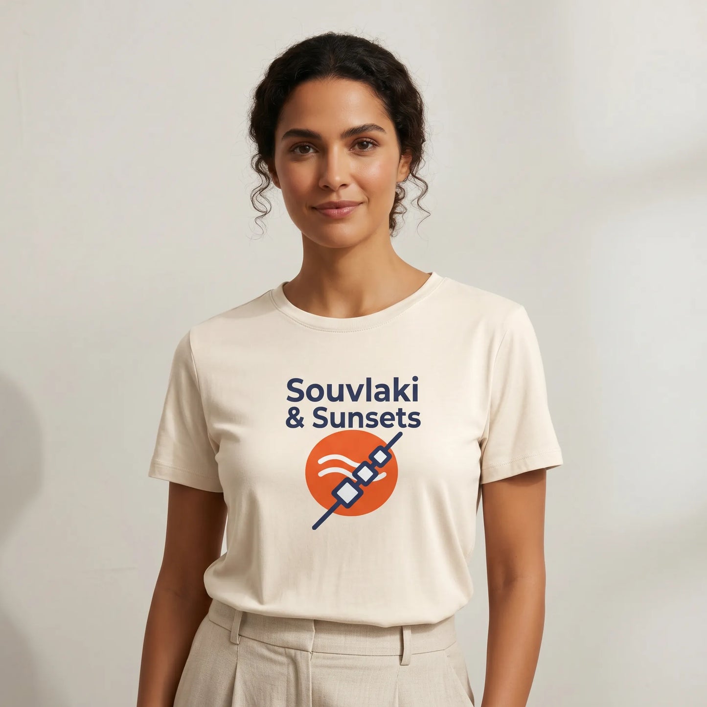 Woman wearing a beige t-shirt with 'Souvliaki & Sunsets' design on a plain background