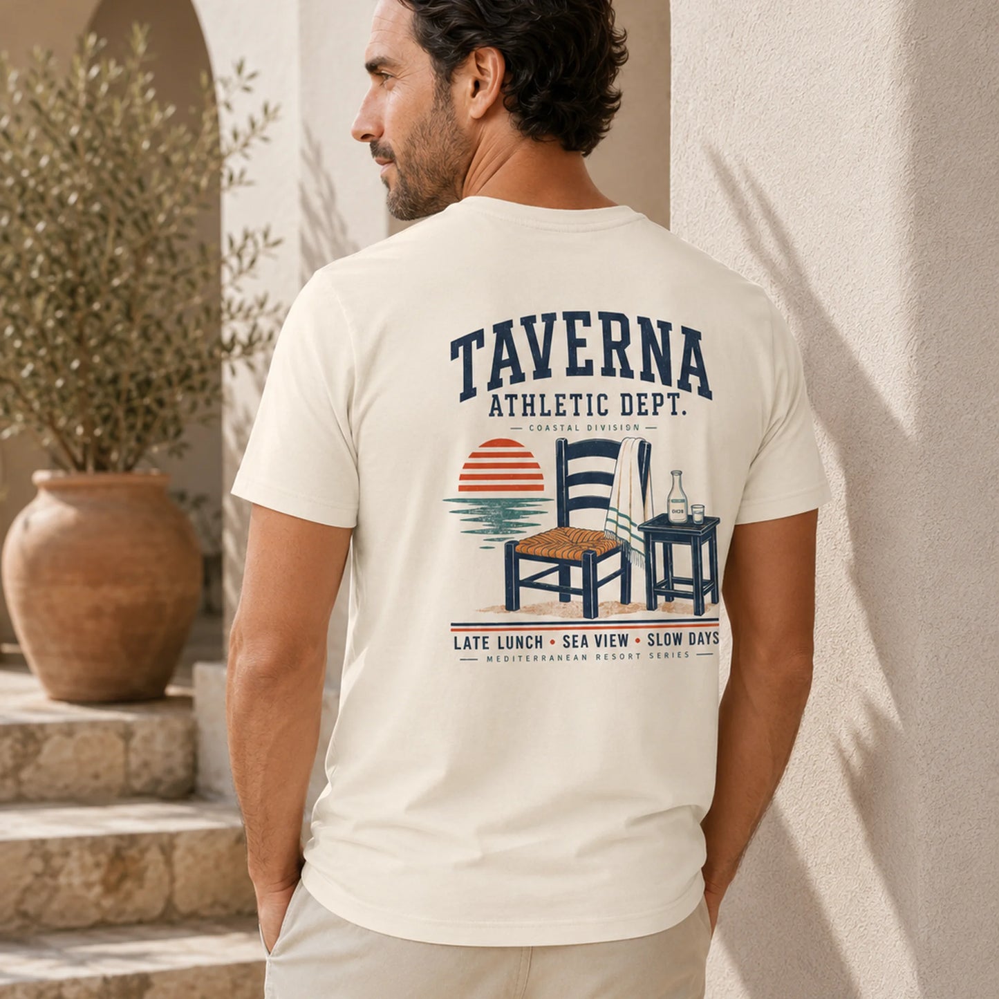 Man wearing a t-shirt with 'Taverna Athletic Dept.' design outdoors.