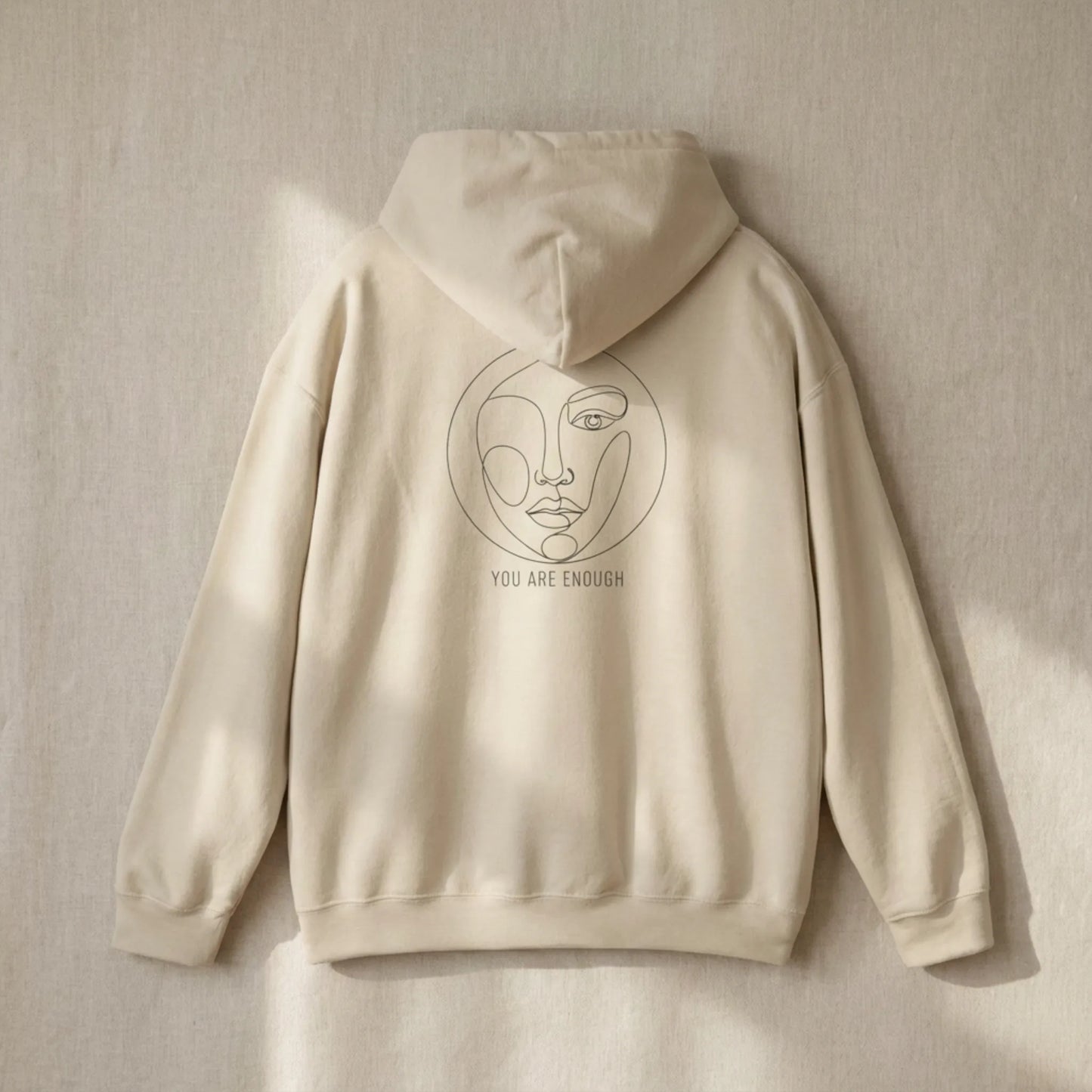 Flat lay of sand Abstract Muse Face hoodie showing full You Are Enough back design