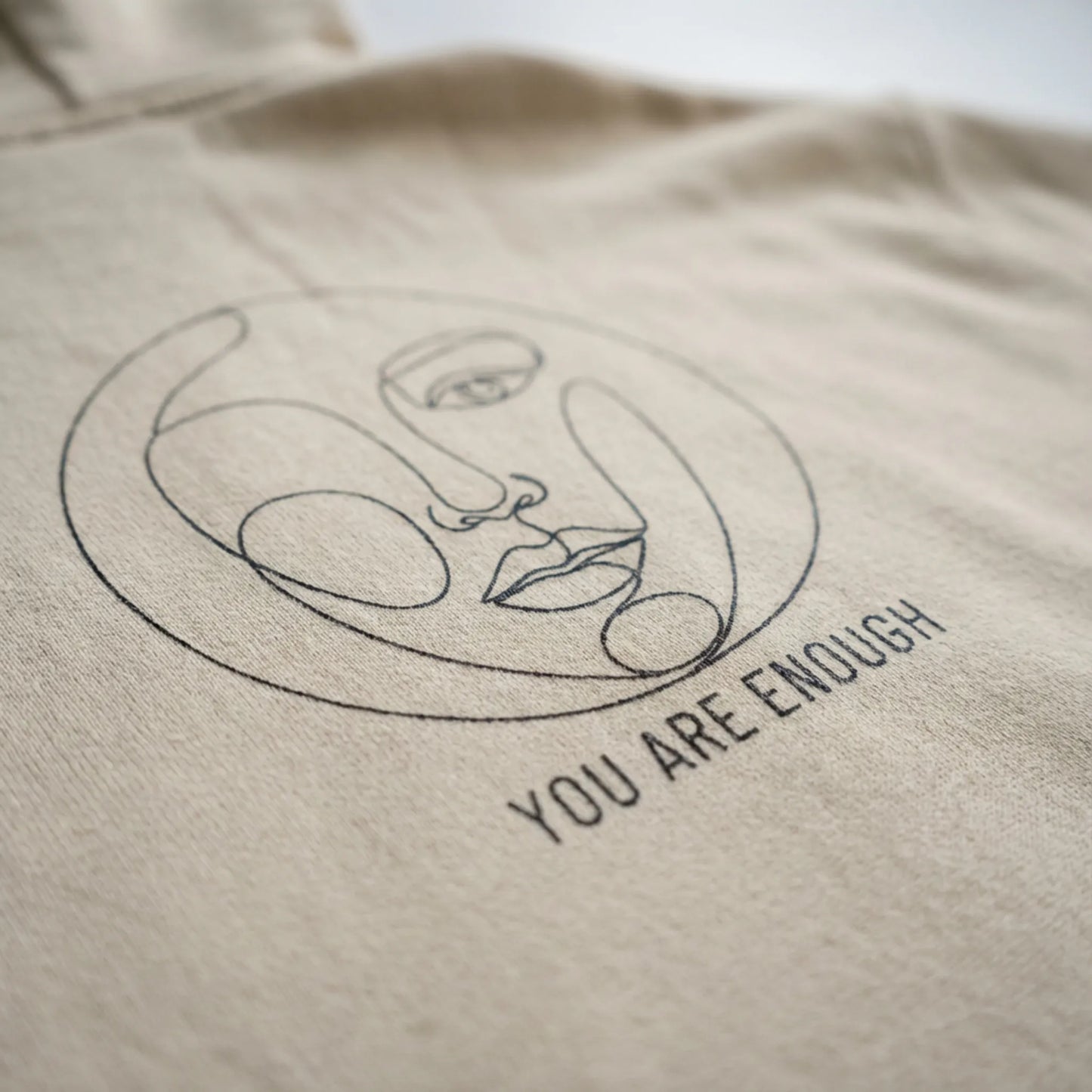 Close-up of Abstract Muse Face and You Are Enough DTG back print on sand hoodie fabric