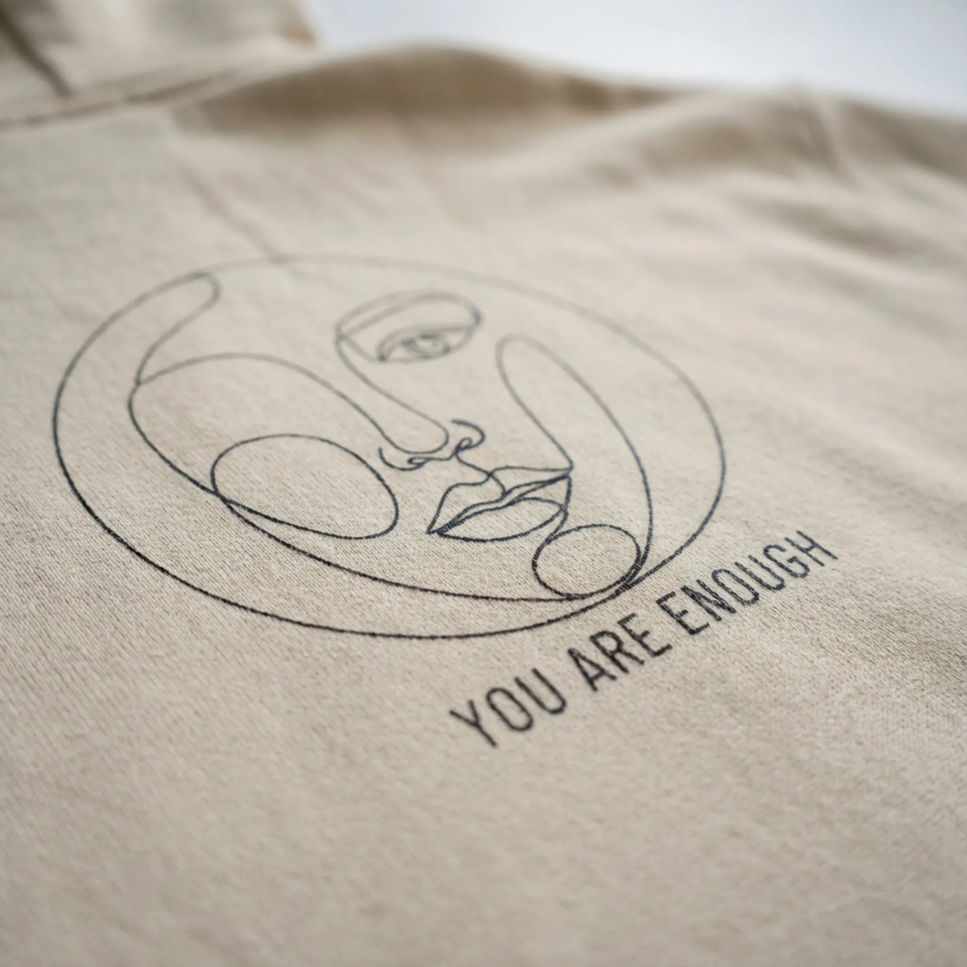 Close-up of Abstract Muse Face and You Are Enough DTG back print on sand hoodie fabric