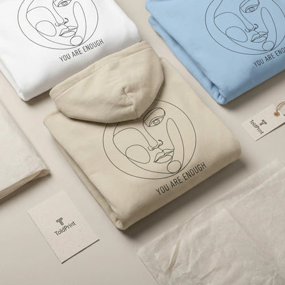 Folded sand Abstract Muse Face hoodie showing part of You Are Enough back design with minimalist ToldPrint packaging