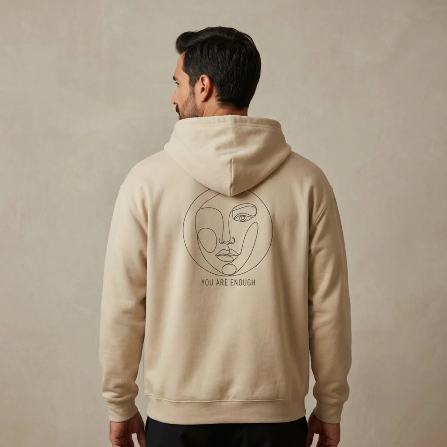 Studio lifestyle image of a μodel wearing sand Abstract Muse Face Ancient Revival hoodie showing You Are Enough back print