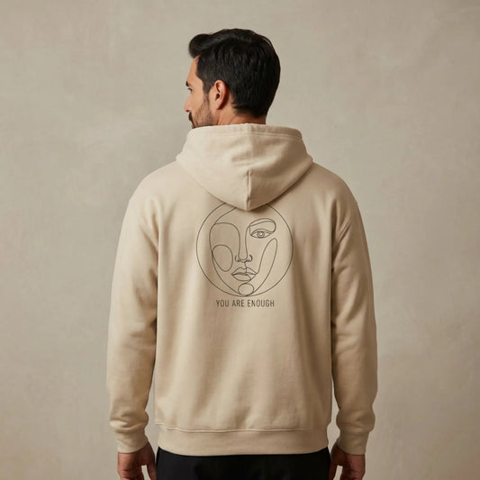 Studio lifestyle image of a μodel wearing sand Abstract Muse Face Ancient Revival hoodie showing You Are Enough back print