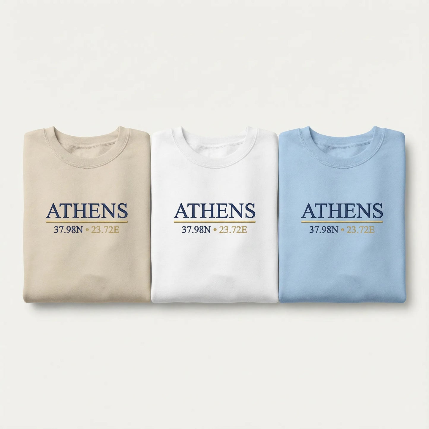 Athens coordinates embroidered crewneck sweatshirt color lineup showing Sand, White, and Light Blue options with navy and gold chest embroidery.