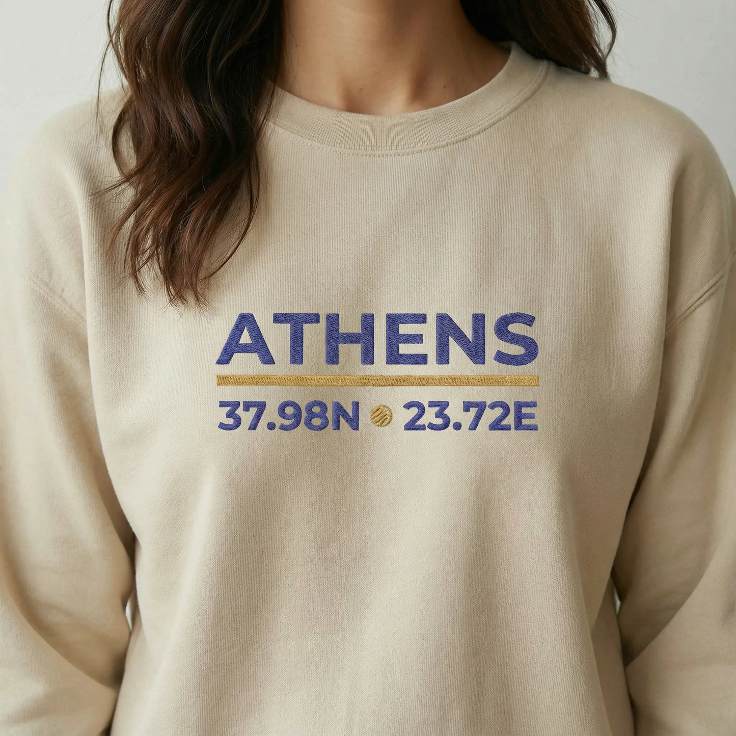 Close-up of Athens coordinates embroidery in navy and gold on sand crewneck sweatshirt