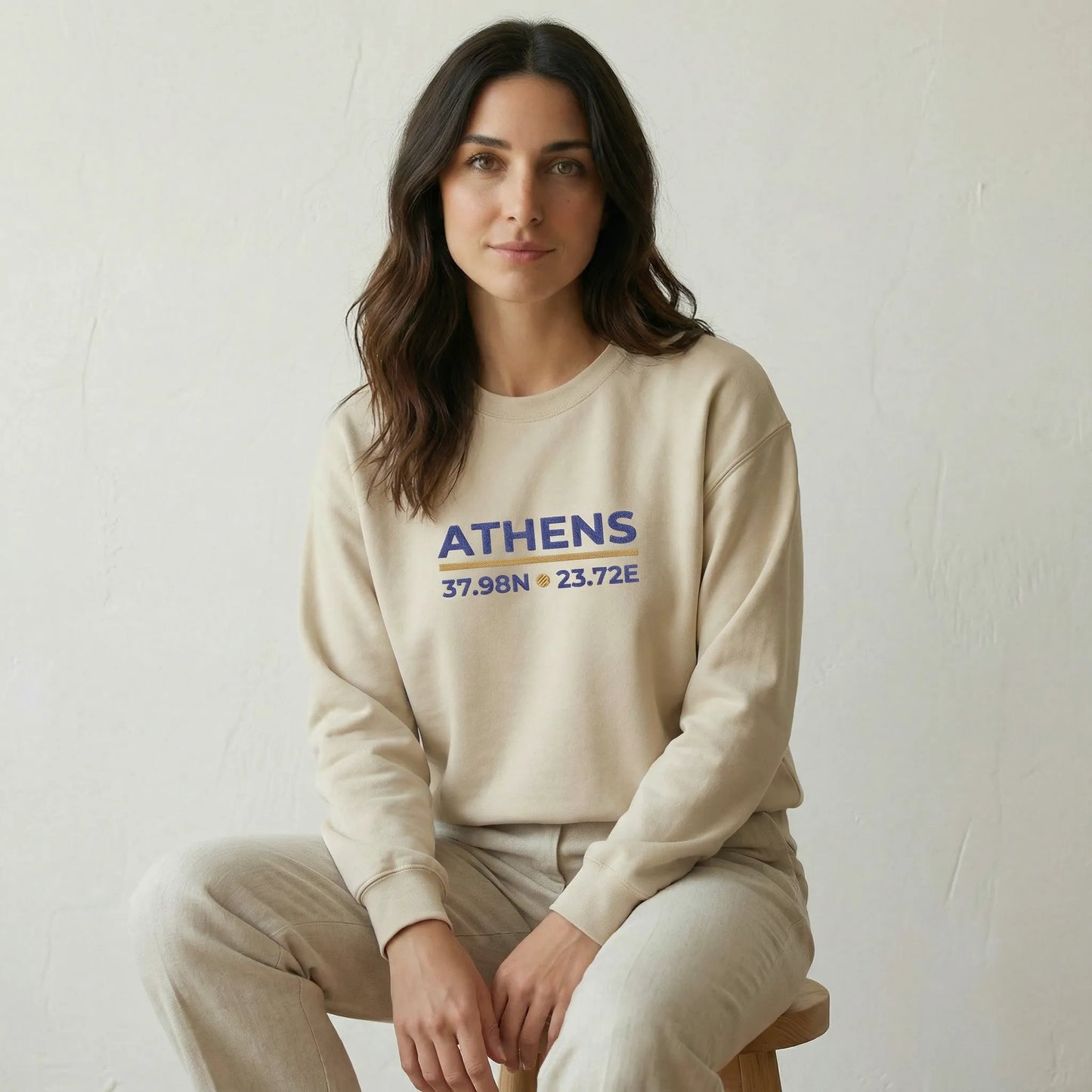 Relaxed seated studio lifestyle shot of model wearing sand Athens embroidered sweatshirt