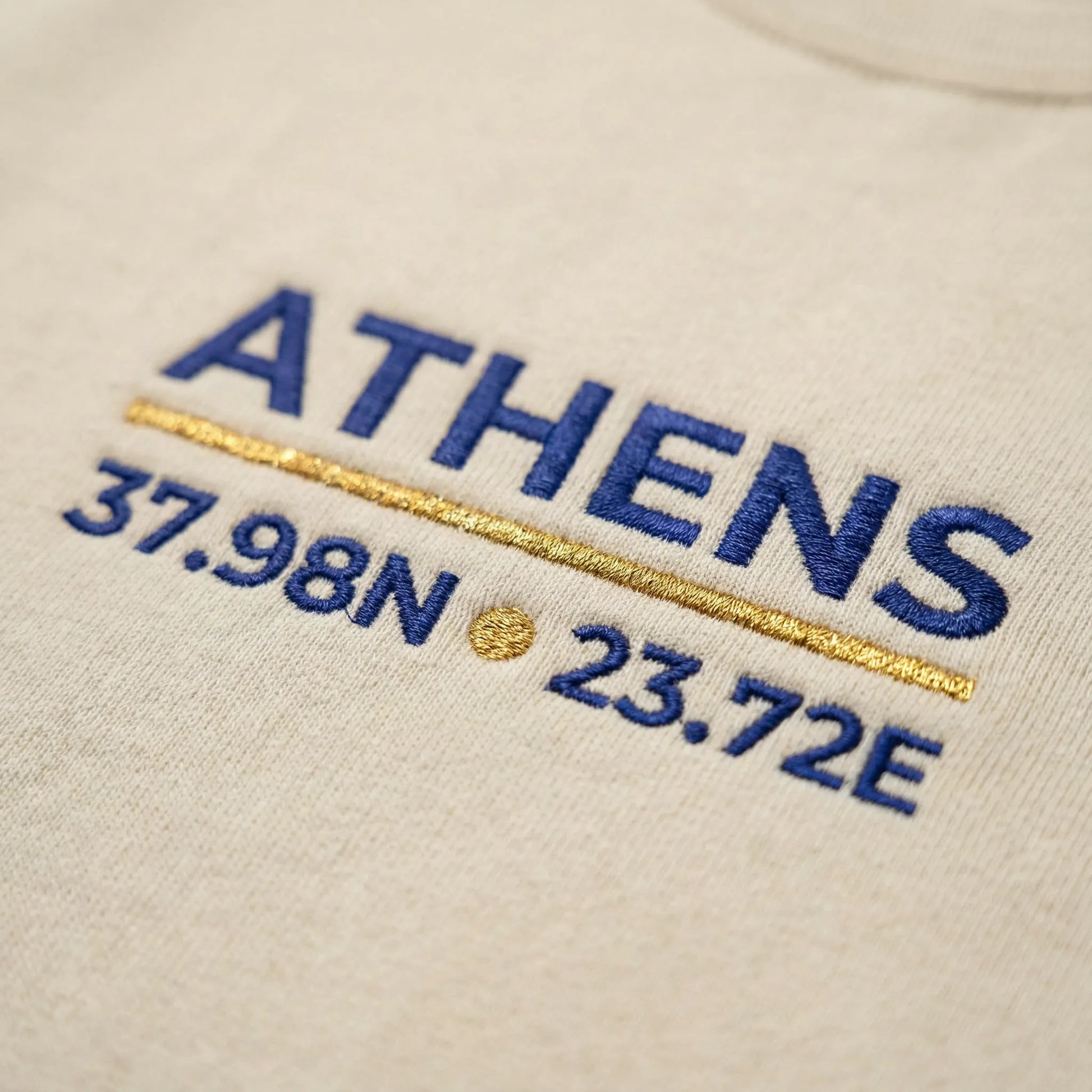 Macro Close-up of Athens coordinates embroidery in navy and gold on sand crewneck sweatshirt