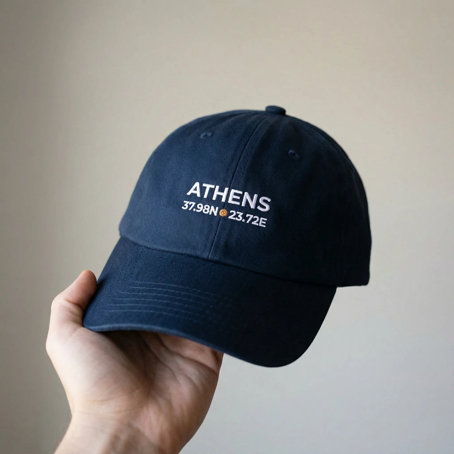 Hand holding Athens coordinates embroidered dad cap for scale.