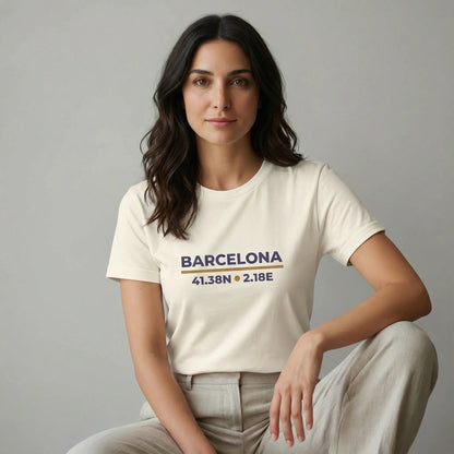 Woman wearing a white t-shirt with 'Barcelona' and coordinates printed on it, sitting against a gray background.